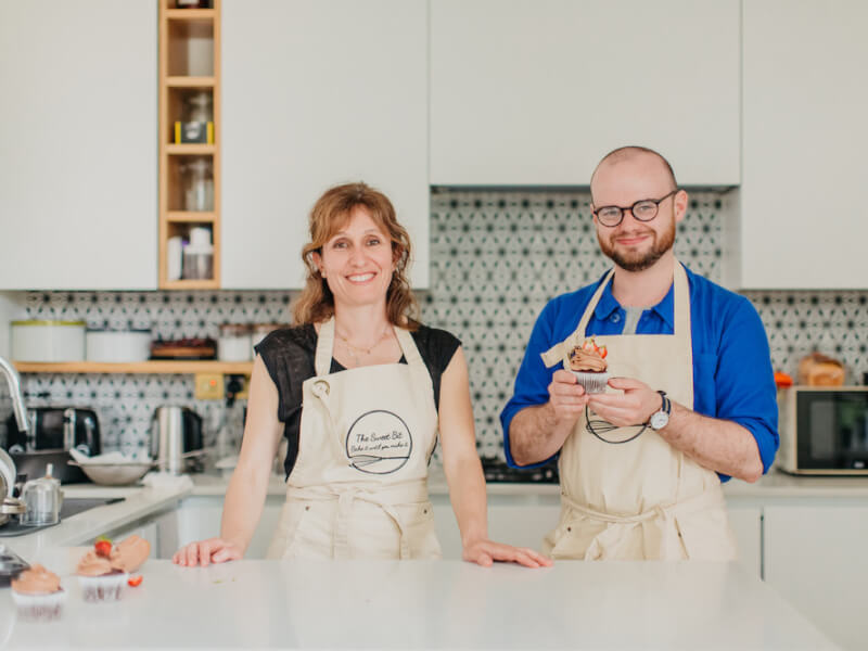 A man and women smile in a kitchen with homemade chocolate cupcakes topped with strawberries